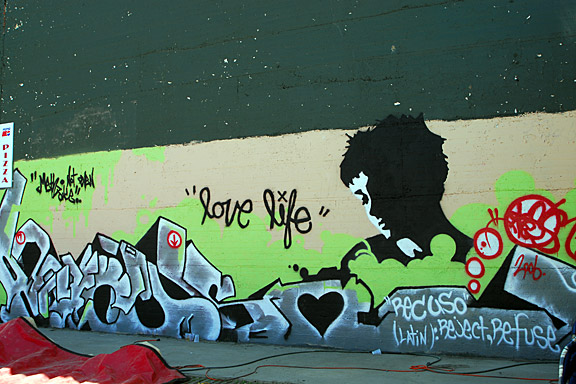 I wanted the art to be something that was very appealing to look at, that had a positive image that people could enjoy. The main image in the painting is large graffiti lettering of the word recuso. Recuso is a latin word meaning: reject, refuse, refuse to; object; decline. (it is obvious why this is a very appropriate.) The second major image in the painting is a stencil of one of my friends. This portion of the painting is focusing more towards beauty in general, it also balances the painting as a whole, as well as adding something powerful and appealing to the eye. The painting in it entirety is supposed to be a positive message more than a negative one. There is a "love life" quote in the center of the painting. love life is a really basic concept that every one can easily relate to on several different levels. My main goal was to portray something that from a distance didn't appear too obvious, in what it's general purpose was. then on closer inspection, the message is easily taken in. I figured if you can get someone to stop and interpret something then it gives them time to think.